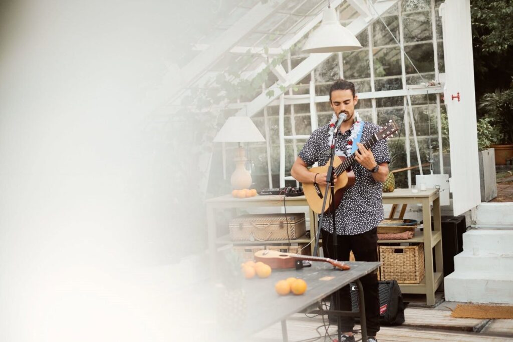 Un guitariste chante devant une serre, une table garnie d’oranges au premier plan